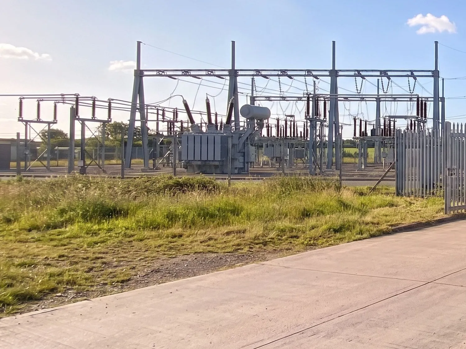Electricity substation compound with a transformer and busbar gantries, and pylons beyond