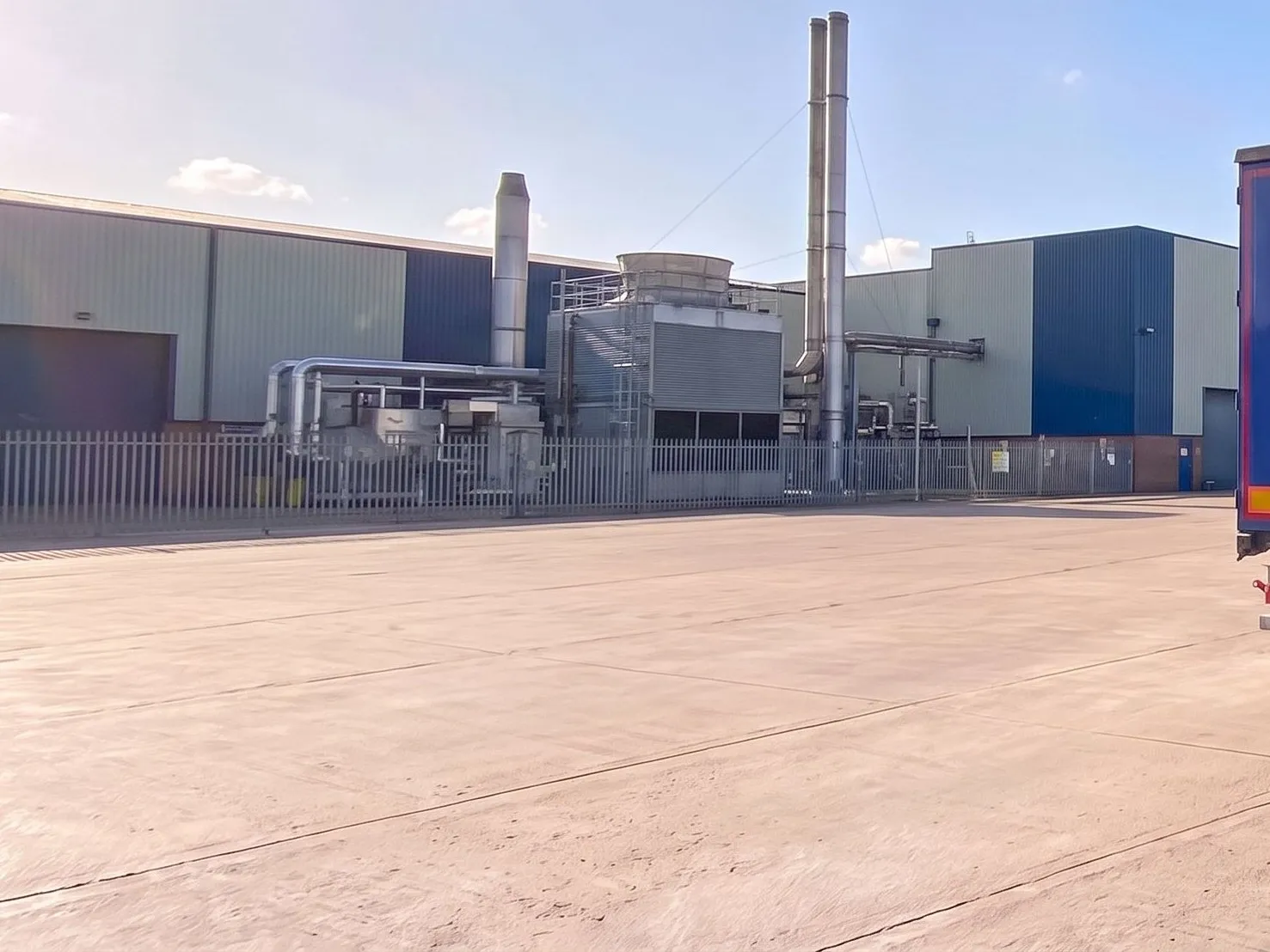 Manufacturing plant yard with process buildings, stacks and pipework beyond the perimeter fence