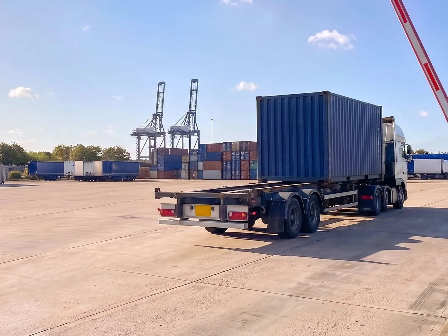Container lorry crossing a port terminal yard towards the quay cranes