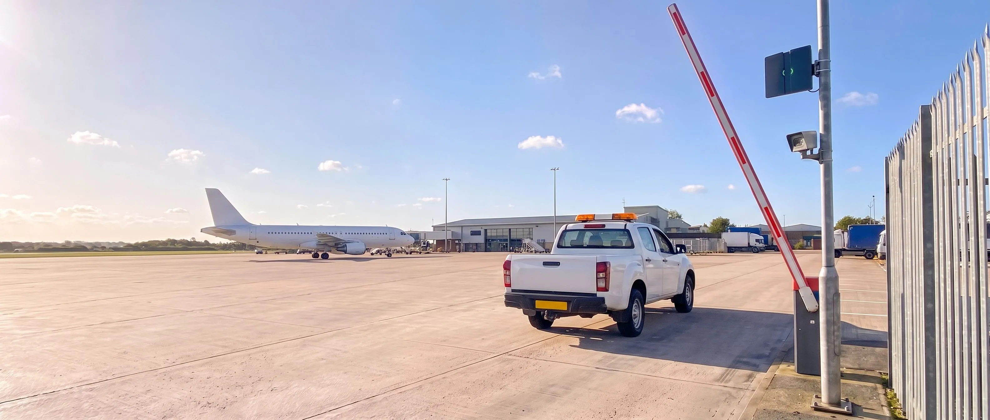 Airfield operations vehicle driving through the raised barrier at an airside access gate, with a Transit Ultimate long-range reader and a camera on the post beside it