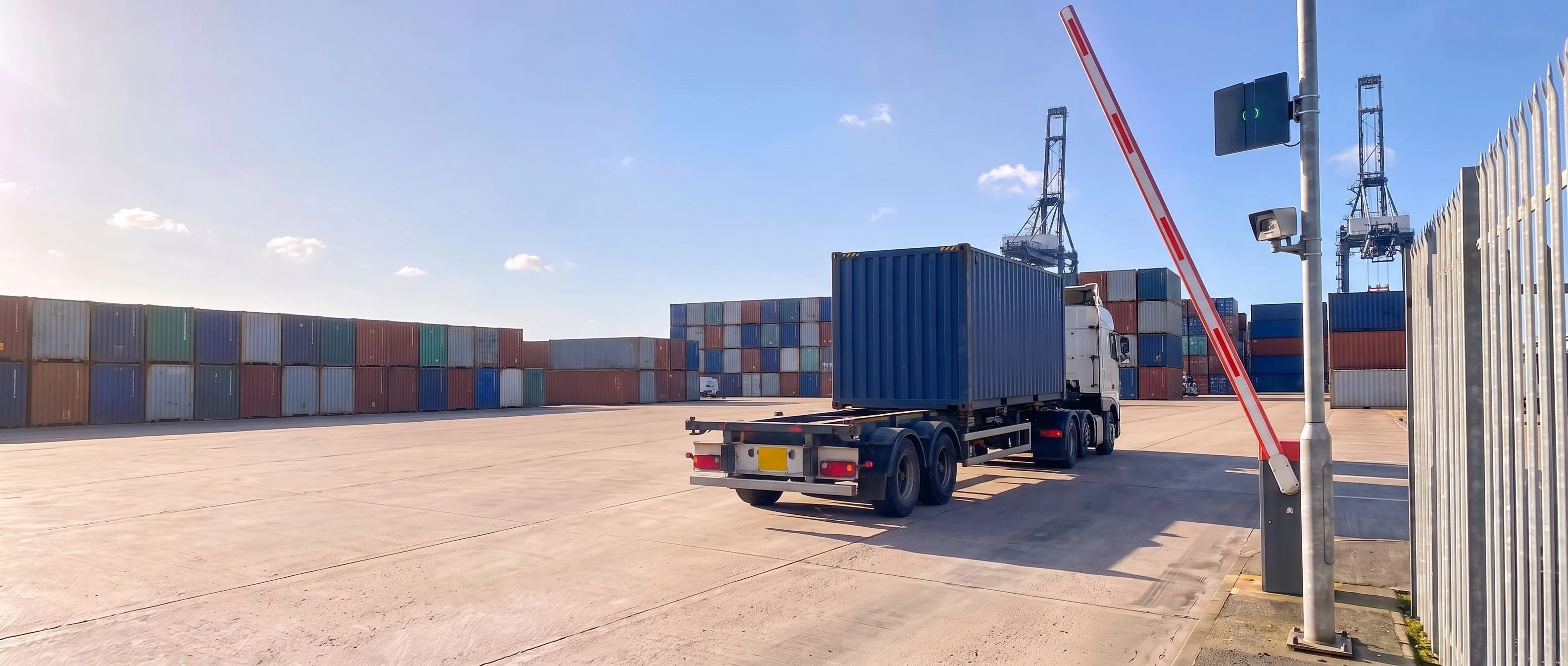 Container lorry driving through the raised barrier at a port terminal gate, with a Transit Ultimate long-range reader and a camera on the post beside it
