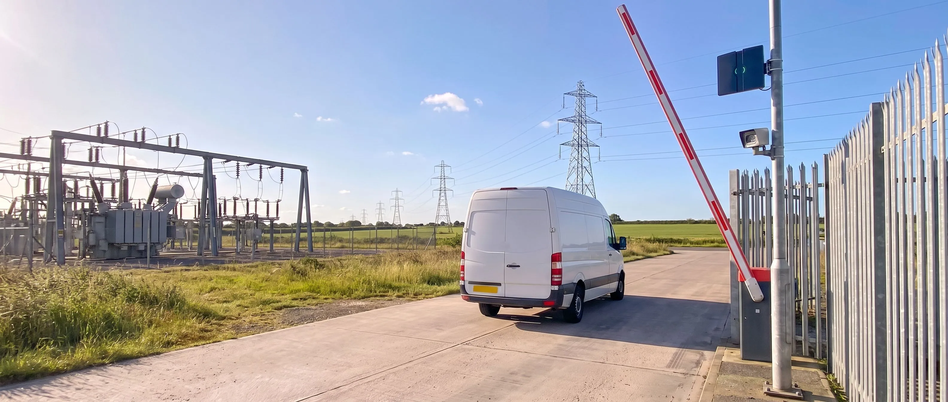 Contractor's van driving through the raised barrier at the unattended gate of an electricity substation, with a Transit Ultimate long-range reader and a camera on the post beside it